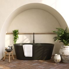 a black bath tub sitting on top of a tiled floor next to a potted plant