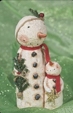 a ceramic snowman with two cats and a christmas tree ornament on a green background