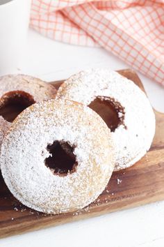 three powdered sugar donuts on a wooden cutting board