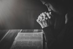 a person sitting in front of an open book with their hands clasped to their face