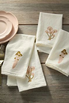 four embroidered napkins with flowers on them next to a pink plate and gold fork