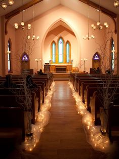 an empty church filled with lots of pews and decorated with branches, lights and candles