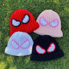 three knitted beanies with eyeballs on them laying in the grass, one is pink and one is blue