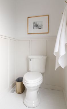 a white toilet sitting in a bathroom next to a gold trash can and framed photograph