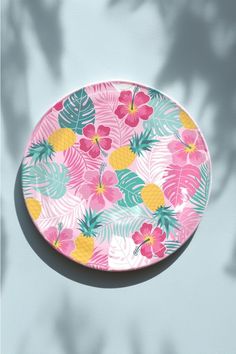 a pink and yellow plate with pineapples, palm leaves and flowers on it