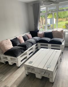 a couch made out of pallets and pillows in a living room next to a window