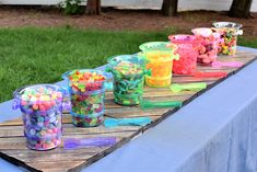 plastic cups filled with candy sitting on top of a wooden table in front of grass