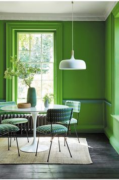 a dining room with green walls, chairs and a table in front of a window