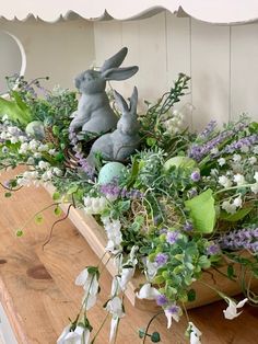 a wooden table topped with a basket filled with flowers and two bunny figurines