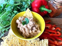 a yellow bowl filled with hummus next to tortilla chips and vegetables on a wooden table