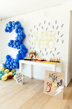 a table topped with balloons and signs next to a wall covered in blue balloon decorations