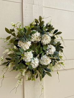 a wreath hanging on the side of a building with white flowers and greenery around it