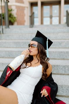 a woman sitting on the steps talking on her cell phone wearing a graduation cap and gown