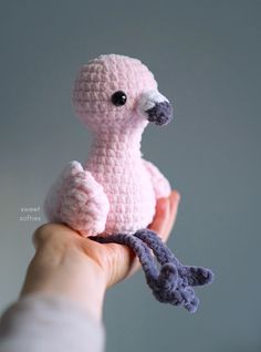 a crocheted pink bird sitting on top of a persons hand holding it in the air