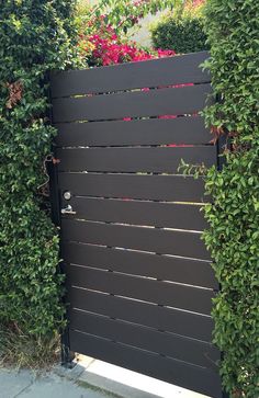 a black gate surrounded by greenery and pink flowers