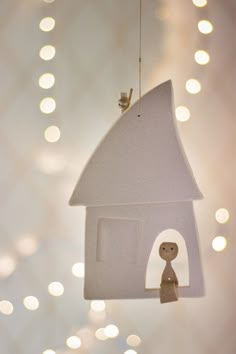 a white birdhouse hanging from a string with a small figure in the bottom right corner