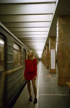 a woman in a red dress is standing next to a train at the subway station