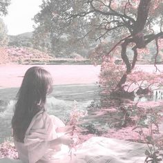 a woman sitting on a blanket next to a tree with pink flowers in the foreground