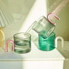 two glass cups sitting on top of a white table next to each other and one has a pink handle