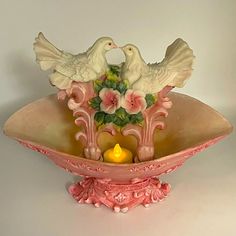 two white doves sitting on top of a pink bowl with a candle in it