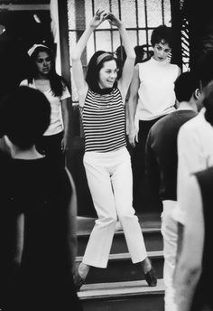 black and white photograph of woman standing on steps with hands in the air, surrounded by other people