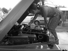 a man working on an engine in the hood of a car at a gas station