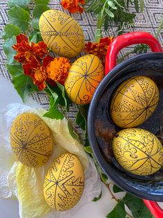 some yellow painted eggs sitting in a bowl next to orange flowers and green leaves on a table