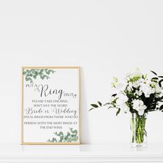 a vase filled with white flowers sitting next to a framed sign that says put your ring on it