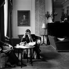 black and white photograph of two people sitting on couches in a room with paintings