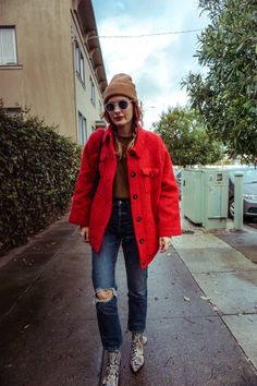 a woman in a red coat and hat walking down the street