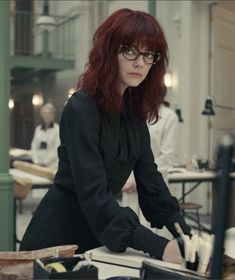 a woman with red hair and glasses sitting at a desk