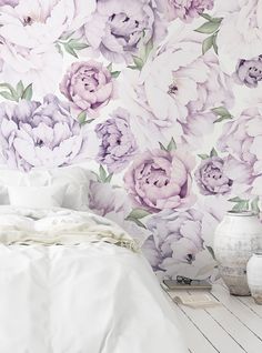 a white bed sitting next to a purple flower wallpaper on a bedroom wall above a night stand