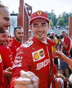 two men in red racing suits are shaking hands with each other while others look on