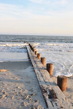 there is a long wooden pier on the beach near the water and waves coming in