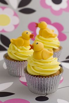 three cupcakes with yellow frosting and little rubber ducks on top are sitting on a polka dot tablecloth