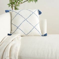 a white couch with a blue and white pillow on top of it next to a potted plant