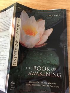 the book of awakeing is open on a table with water droplets and a pink flower