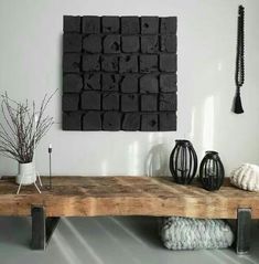 a wooden table topped with black vases next to a wall mounted art piece on a white wall