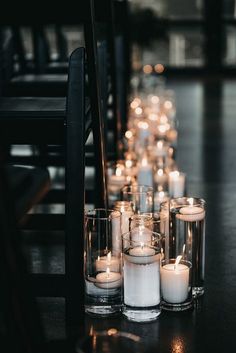 candles are lined up on the floor next to each other in glass vases and chairs