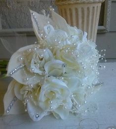 a bridal bouquet with white flowers and pearls on the side of a wall next to a flower pot