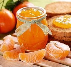 an orange jam in a glass jar next to sliced bread and tangerines on a cutting board