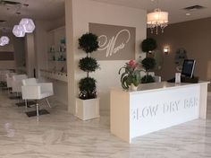 the inside of a salon with white chairs and flowers in vases on the counter