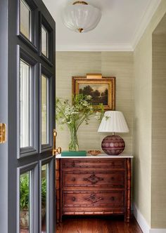 an entry way with a dresser, lamp and painting on the wall behind glass doors