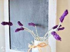 purple flowers are in a white vase on a table next to an old window frame