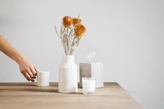 a person is arranging flowers in vases on a wooden table with two glasses and a candle holder