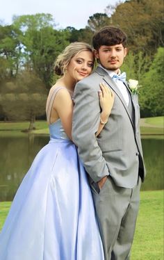 a young man and woman in formal wear posing for a photo by a lake with their arms around each other