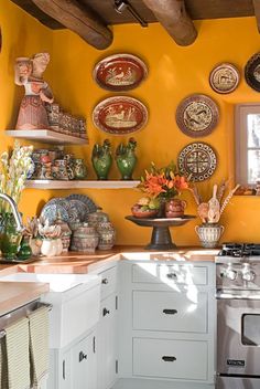 a kitchen with yellow walls and lots of plates hanging on the wall above the stove