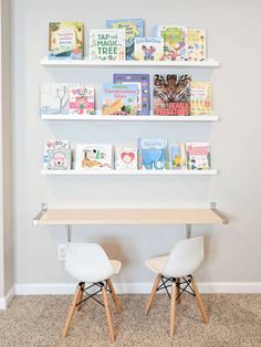 two white chairs sitting in front of a wooden table with books on the shelves above it