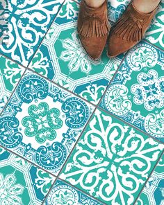 someone's feet in brown shoes standing on a blue and white tile floor with an ornate pattern