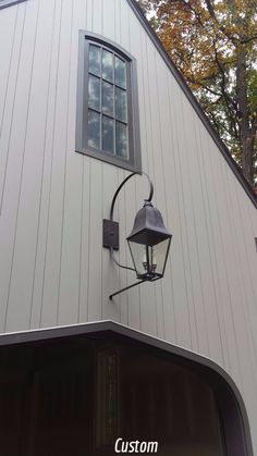 an old fashioned light hanging from the side of a white building with trees in the background